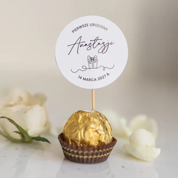 Winietki na roczek umieszczone na czekoladkach Ferrero Rocher z ozdobnym napisem i grafiką prezentu.