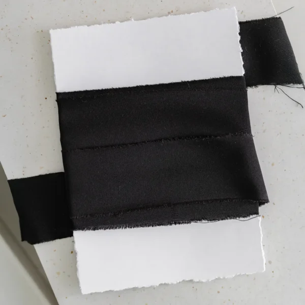 Czarna wstążka satynowa owinięta wokół białej kartki o postrzępionych brzegach.