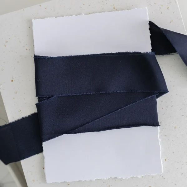 Granatowa wstążka satynowa owinięta wokół białej kartki o postrzępionych brzegach.