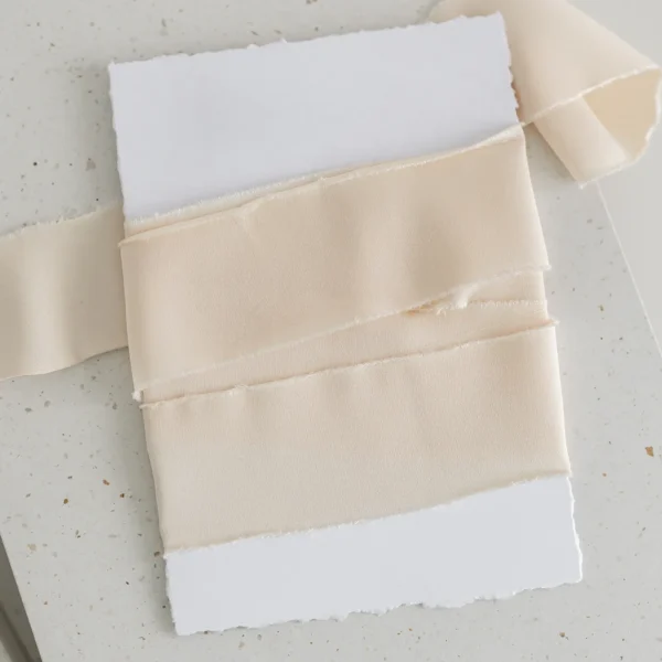Jasnobeżowa wstążka satynowa owinięta wokół białej kartki o postrzępionych brzegach.