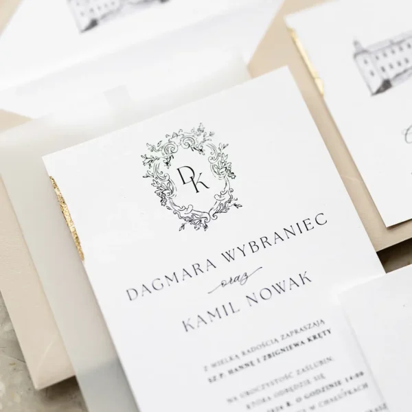 Zbliżenie na zaproszenie ślubne z kolekcji Zamek Chałupki z ozdobnym monogramem i złoconymi brzegami, widoczne koperty i wkładka z rysunkiem zamku