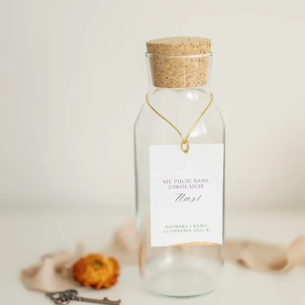 Szklana butelka z korkiem, ozdobiona zawieszką z napisem „Nie pijcie sami, zawołajcie nas!” i złotym sznurkiem, z kolekcji Zamek Chałupki