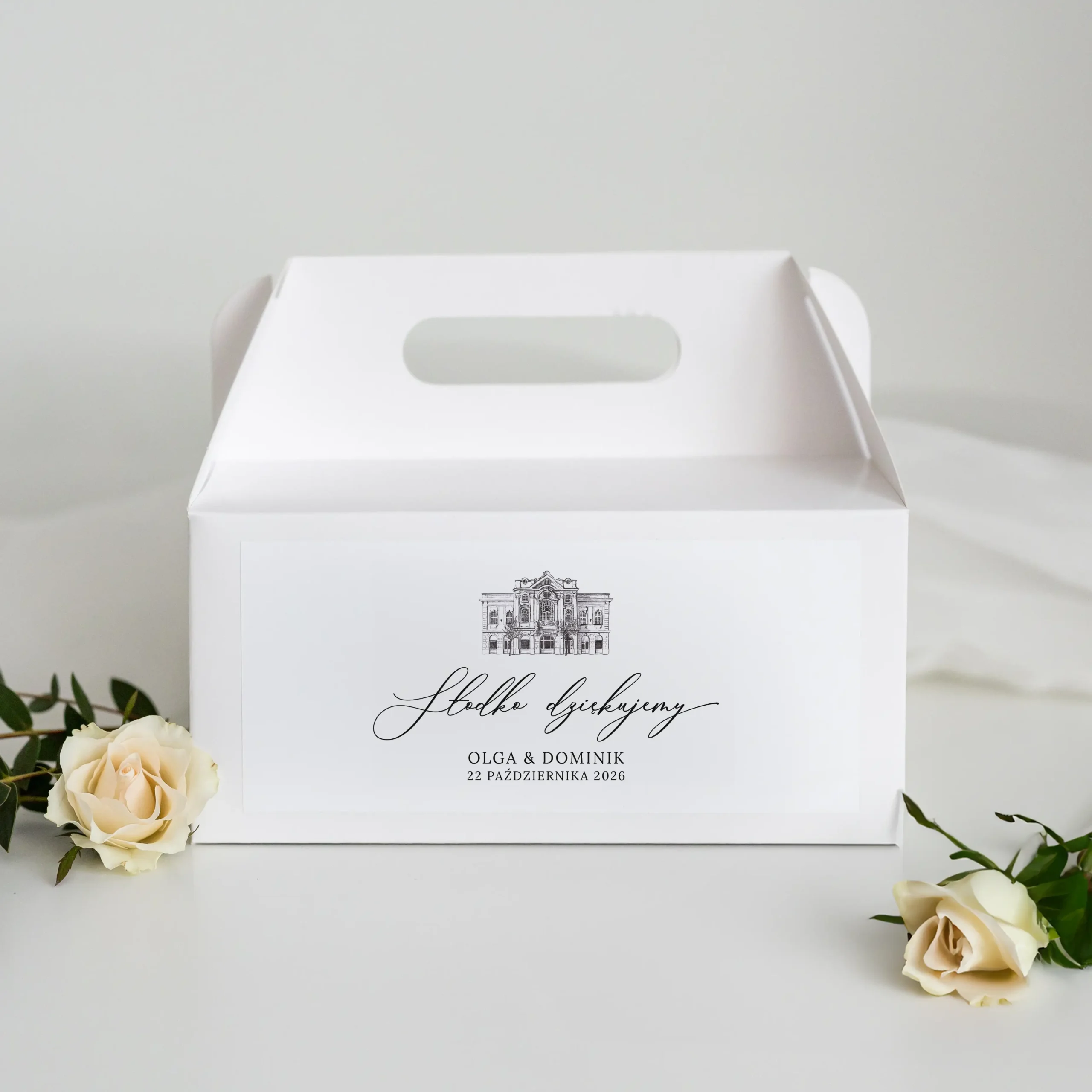 Białe pudełko na ciasto weselne z rysunkiem Hotelu Pod Zielonym Dębem i napisem „Słodko dziękujemy”, imionami Olga i Dominik