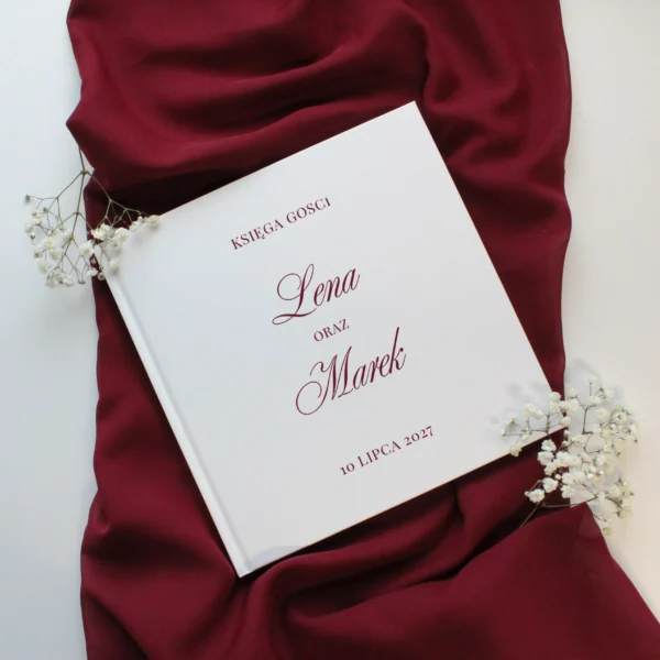 księga gości Burgund z imionami w bordowym kolorze, ułożona na bordowej tkaninie z gałązkami gipsówki.