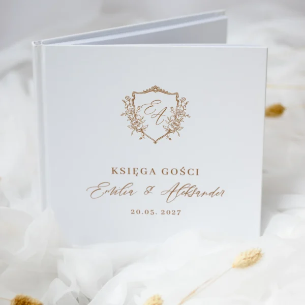 iała księga gości ślubnych z monogramem i złotym napisem, sfotografowana pod kątem, ułożona na tiulu.