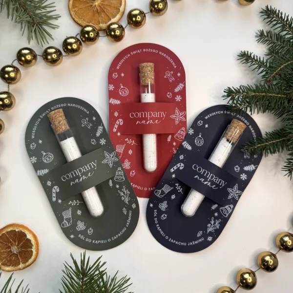 zestaw trzech świątecznych soli do kąpieli w kolorach czerwonym, zielonym i granatowym ułożonych na tle złotych bombek i gałązek świerku