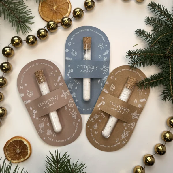 zestaw świątecznych soli do kąpieli w ekologicznych opakowaniach w kolorach beżowym, niebieskim i brązowym na tle gałązek i suszonych pomarańczy