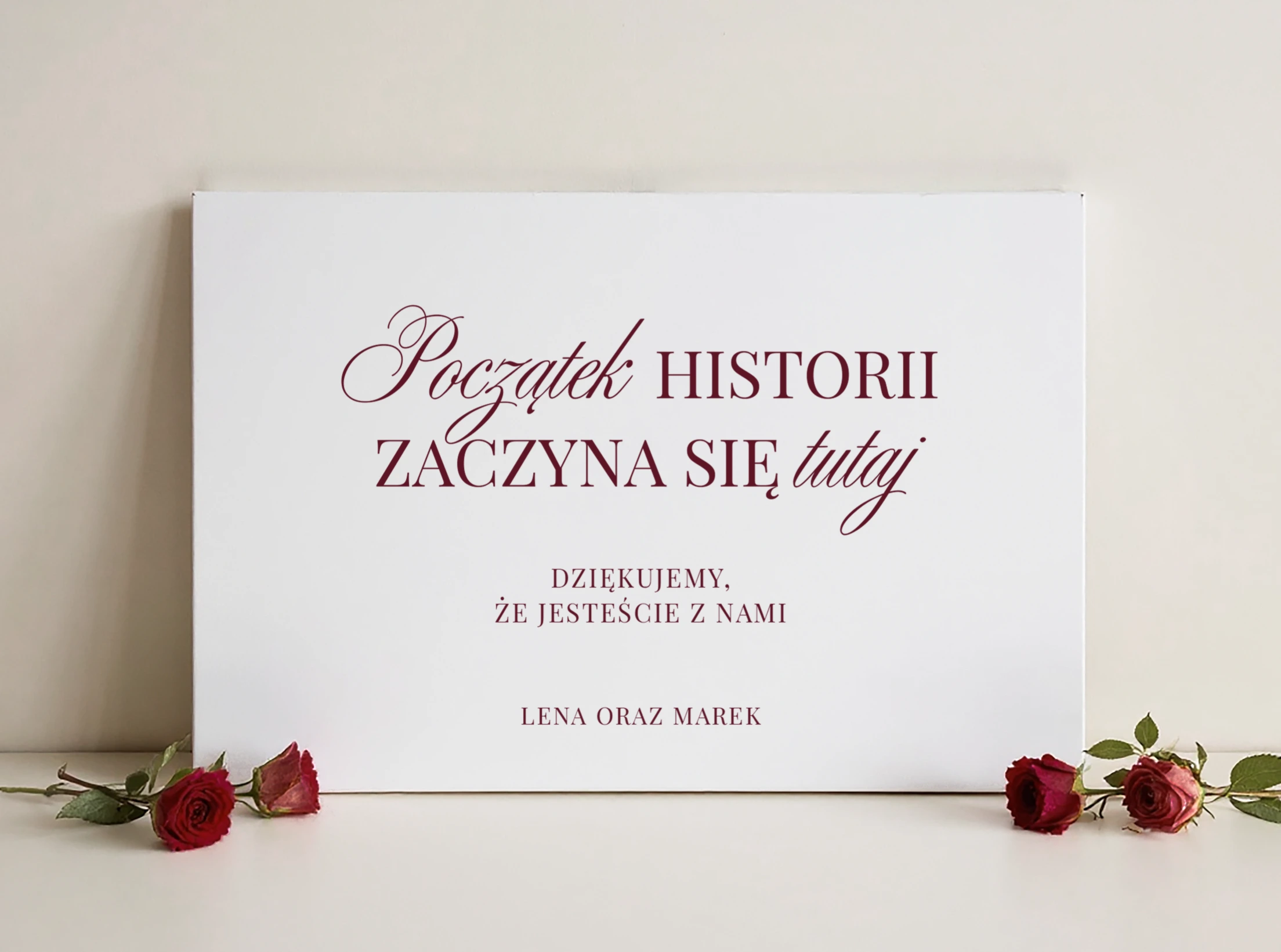 tablica powitalna burgundowa z napisem „Początek historii zaczyna się tutaj” w otoczeniu czerwonych róż