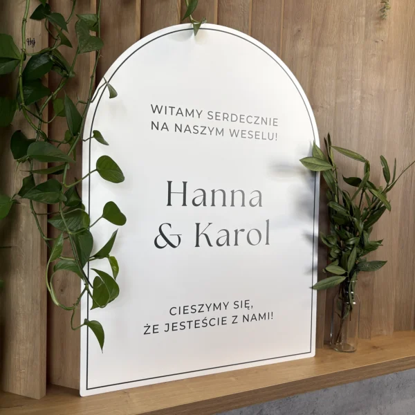 ablica powitalna Jungle w formie łuku, w minimalistycznym stylu z ciemnozielonym napisem i delikatnymi roślinnymi akcentami.