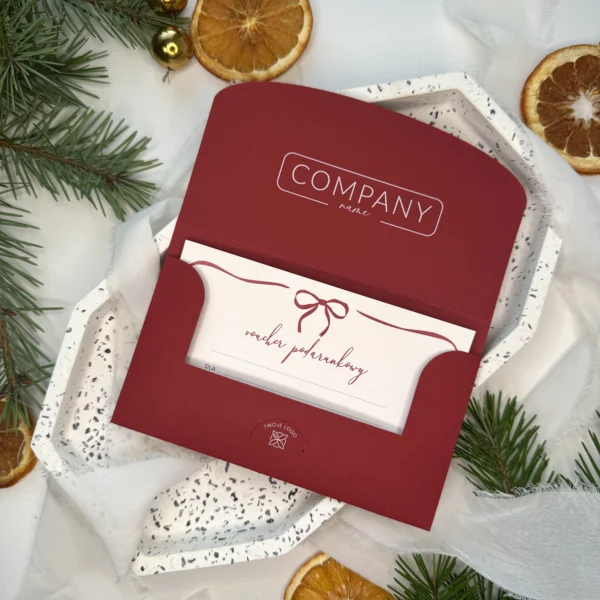 bordowy voucher świąteczny z kokardką i miejscem na logo firmy na tle gałązek świerku i suszonych pomarańczy
