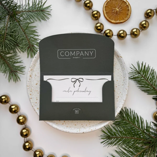 otwarty zielony voucher świąteczny z kartą podarunkową i kokardką na tle złotych bombek