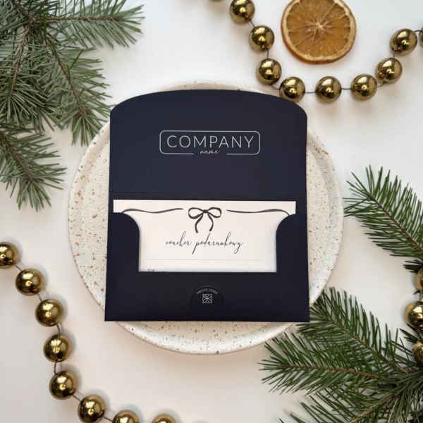otwarty granatowy voucher świąteczny z kartą podarunkową i kokardką w otoczeniu świątecznych ozdób
