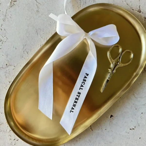 pojedyncza winietka kokardka z imieniem gościa na białej wstążce, zawiązana na złotej tacy.