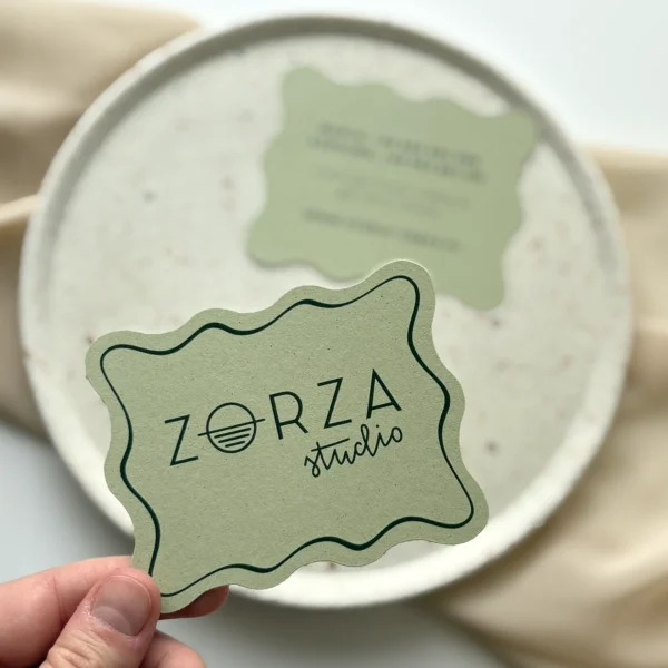 Wizytówki Zorza Studio w nieregularnej formie, prezentujące logo i dane kontaktowe na zielonym papierze.