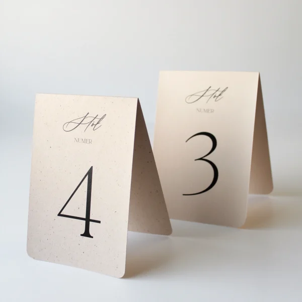 Numery kremowe beżowy z drobinkami i ciasteczkowy, dwa numery stołów w formie daszków, zestawienie kolorów kolekcji kremowej na jasnym tle