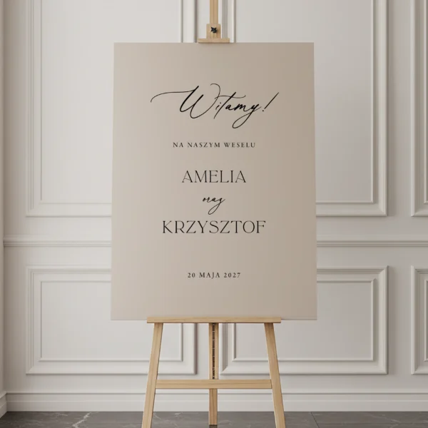 beżowa tablica powitalna z napisem „Witamy” ustawiona na drewnianej sztaludze, minimalistyczna typografia, jasne wnętrze z klasyczną sztukaterią w tle