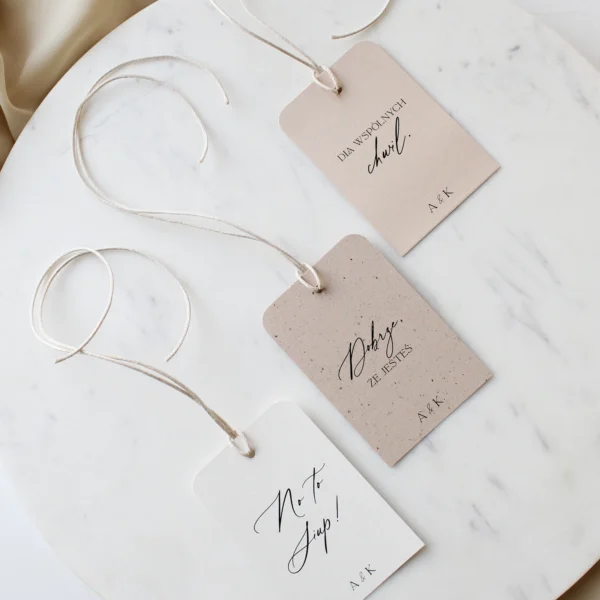 Zawieszki na alkohol w kremowej kolorystyce z jasną wstążką szyfonową ułożone na marmurowym tle