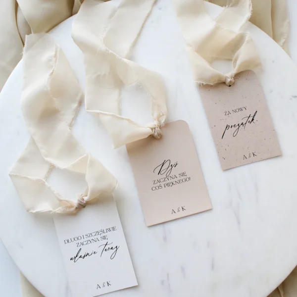 Zawieszki na alkohol w kremowej kolorystyce z jasną wstążką szyfonową ułożone na marmurowym tle