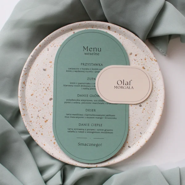 menu weselne Eukaliptus w odcieniu matcha w kształcie łuku z dopasowaną winietką, ułożone na jasnym talerzu