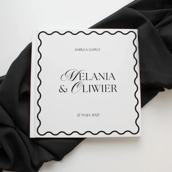 Księga gości z kolekcji Wave z czarnym napisem i ozdobną ramką, sfotografowana na tle czarnej tkaniny