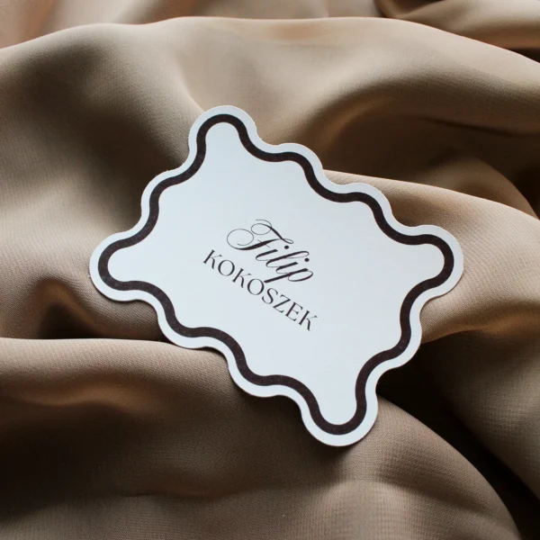 Winietka w brązowym kolorze, leżąca na beżowej tkaninie, z kontrastowym brzegiem.