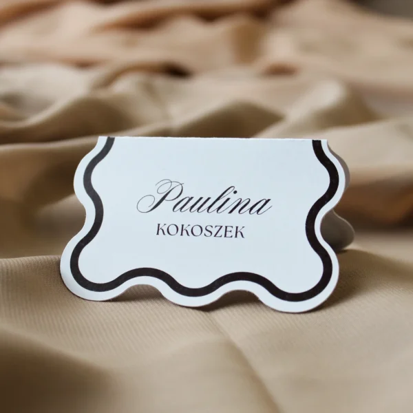 Stojąca winietka z kolekcji Modern Wave w wersji brązowej, na tle jasnobeżowej tkaniny.