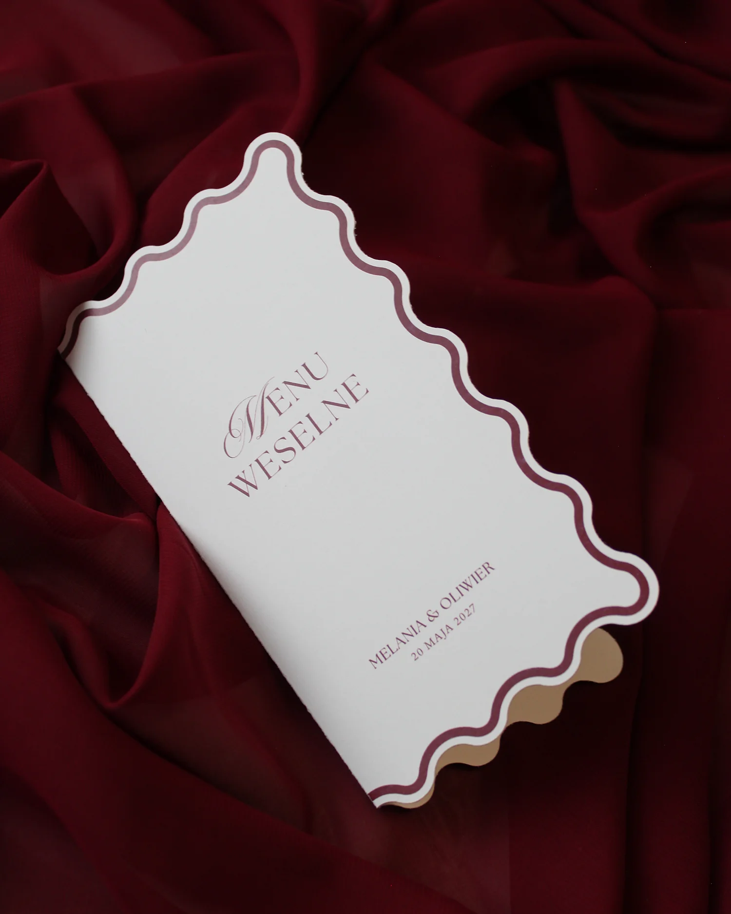 bordowe menu weselne z falowanym brzegiem na bordowej tkaninie