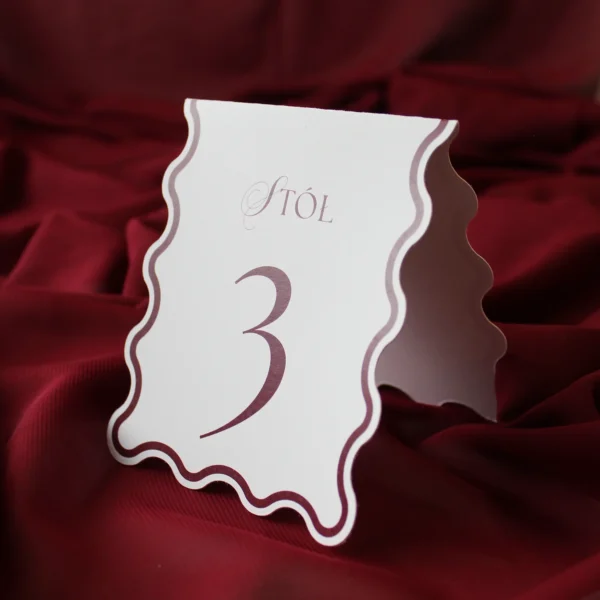 stojący numer stołu z bordowym nadrukiem, widoczny z boku na czerwonym tle