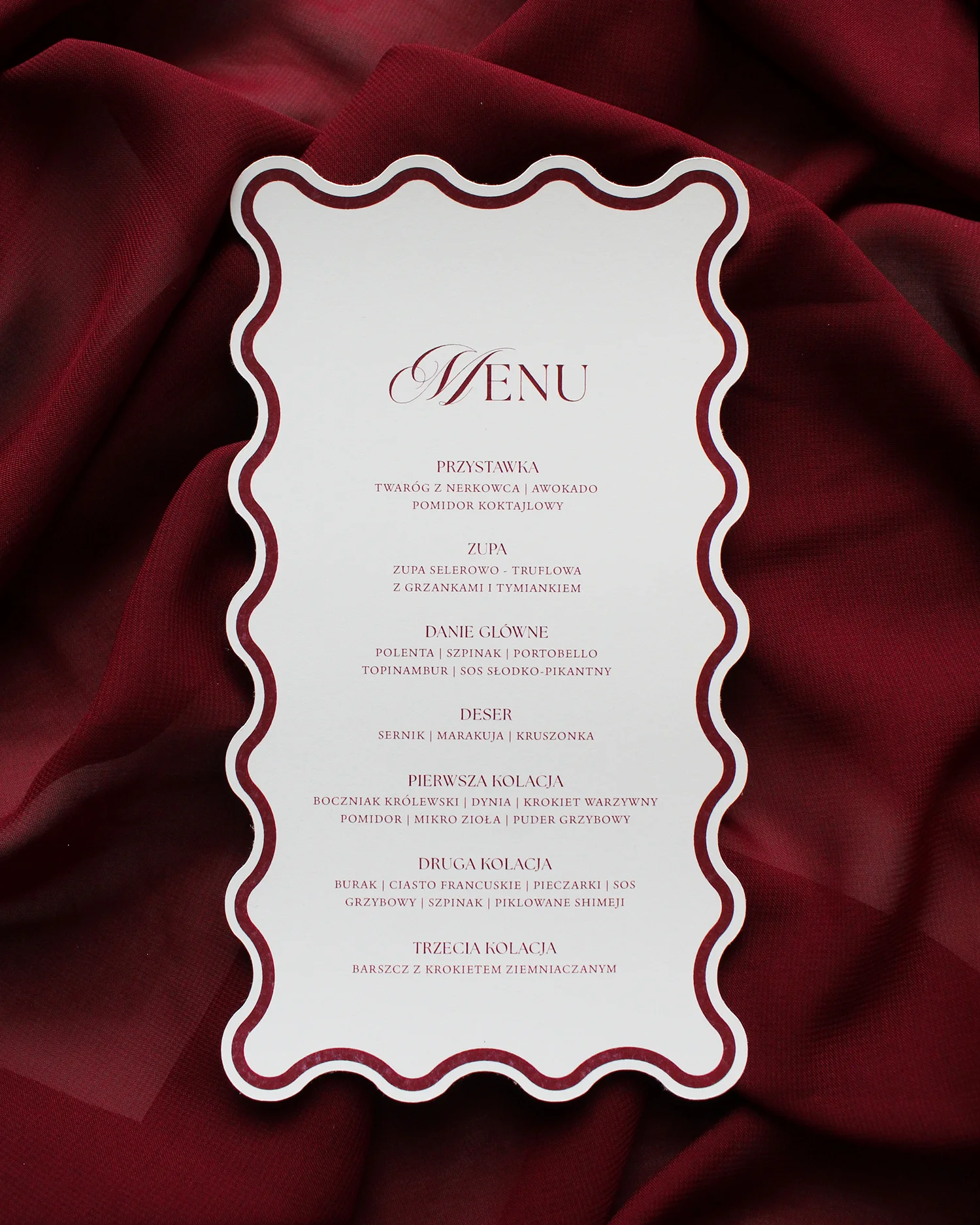 Menu weselne z bordową ramką i falowanymi krawędziami, na tle bordowego materiału