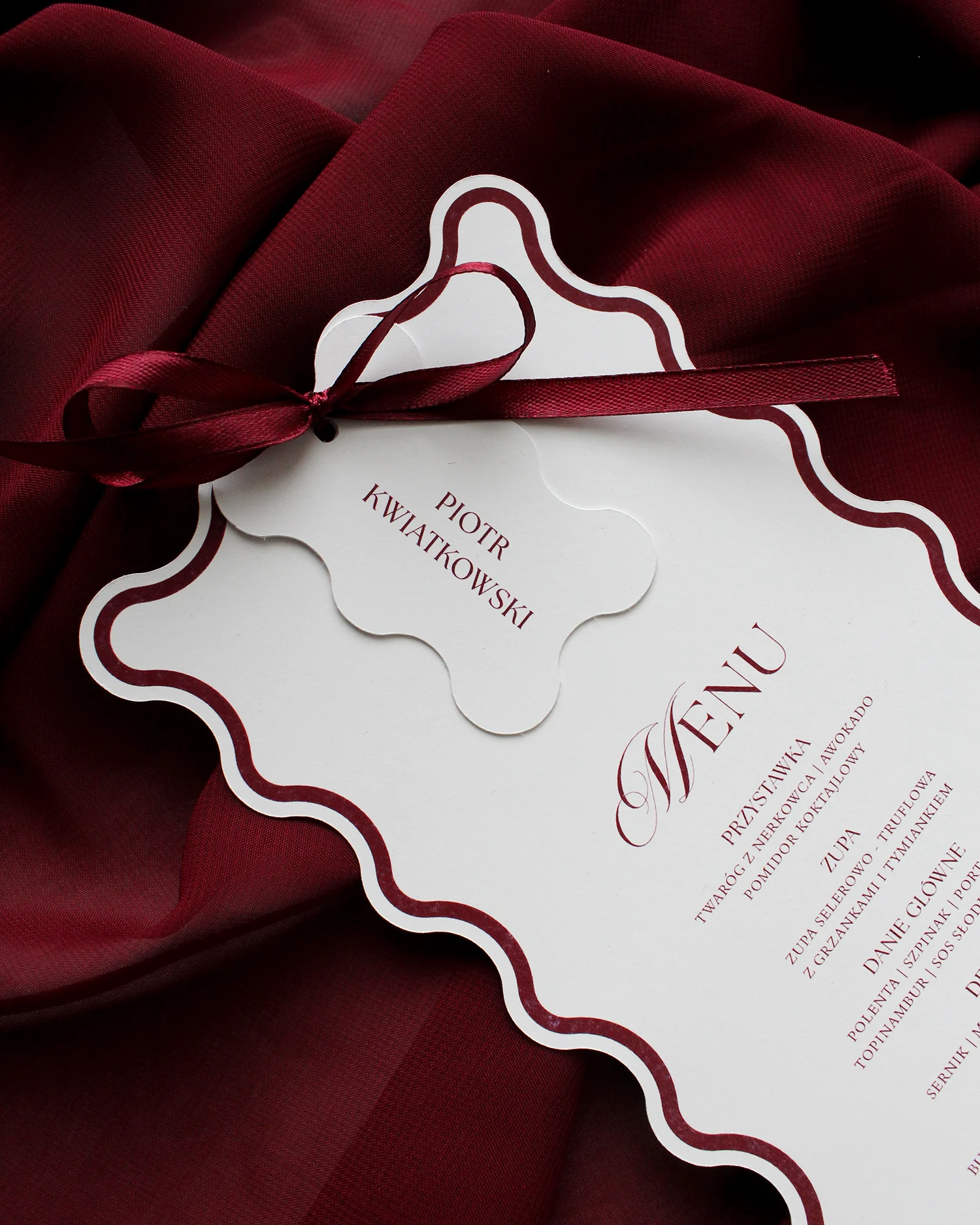 Menu weselne z bordową kokardką i dopasowaną winietką, oba elementy z falowanym brzegiem.