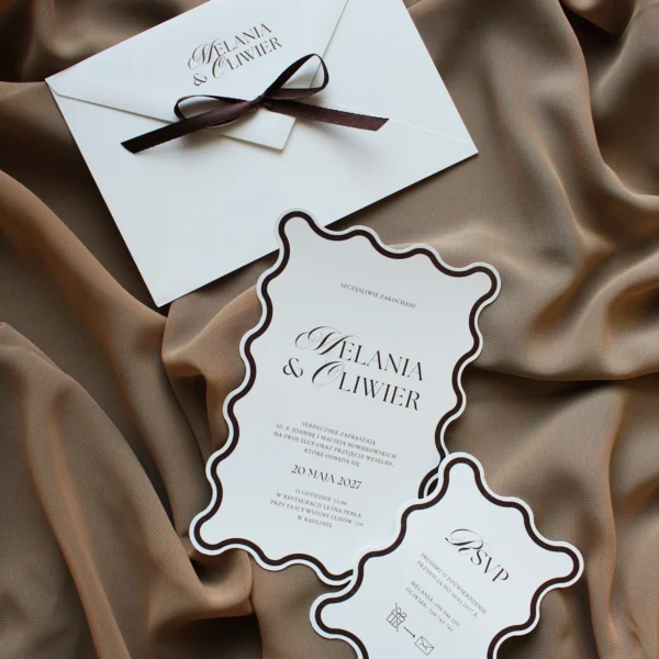 Zaproszenie i RSVP z kolekcji Modern Wave w brązowej oprawie, ułożone na beżowej tkaninie.