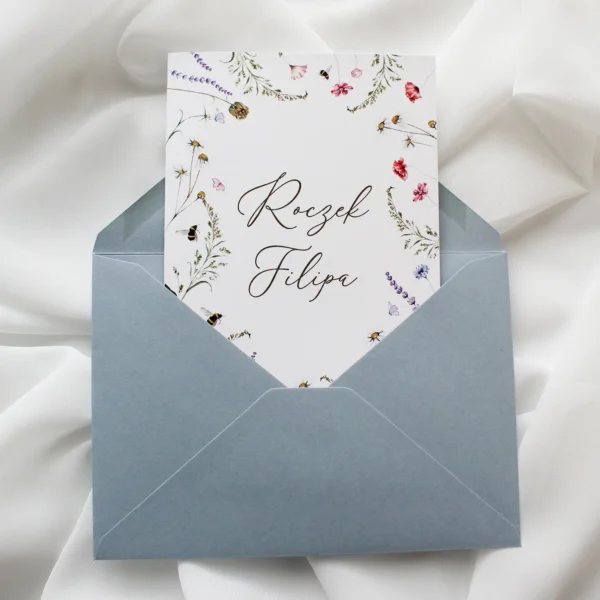 Zaproszenie na roczek polne kwiaty w niebieskiej kopercie z ilustracją kwiatów