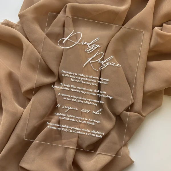 zaproszenie dla rodziców na plexi z eleganckim białym napisem na tle beżowej tkaniny