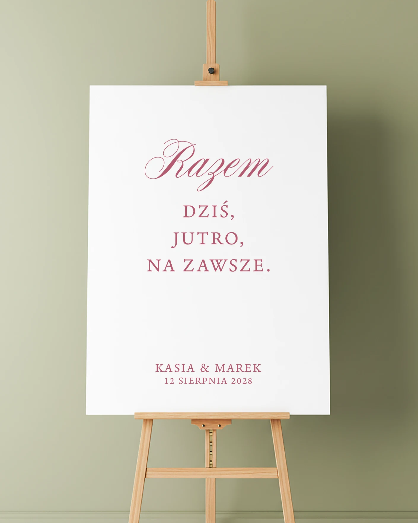 Tablica powitalna z kolekcji Forest na drewnianej sztaludze, z napisem „Razem dziś, jutro, na zawsze” w ciemnoróżowym kolorze, na tle oliwkowozielonej ściany.