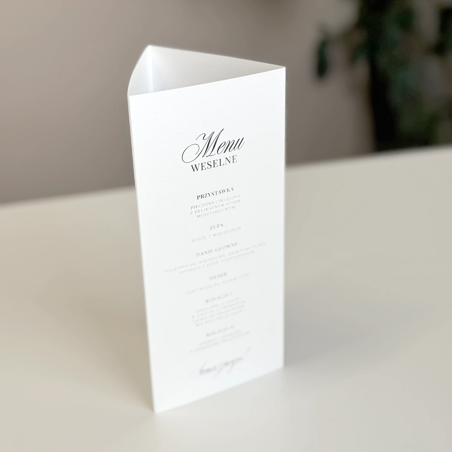 Stojące trójkątne menu z harmonogramem wesela, numerem stołu i minimalistycznym czarnym drukiem.