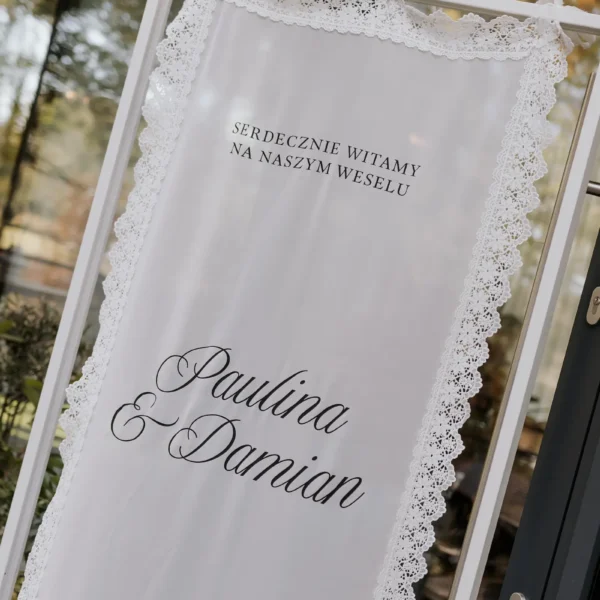 Zbliżenie na tablicę powitalną na tkaninie z ozdobną koronką i czarnymi napisami